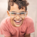 Brunette boy with glasses smiles after getting dental sealants to prevent tooth decay and cavities