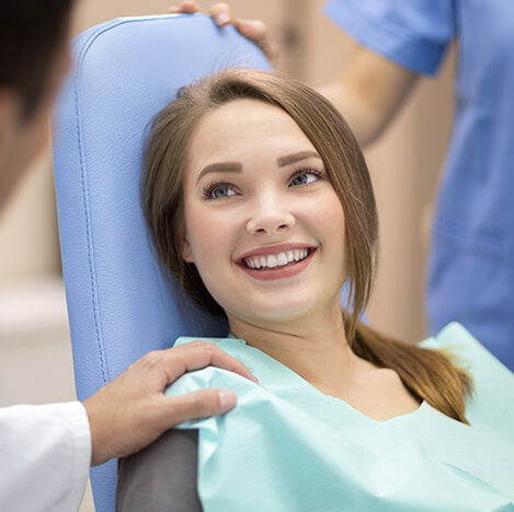 smiling girl sitting in a dental chair, speaking with her dentist